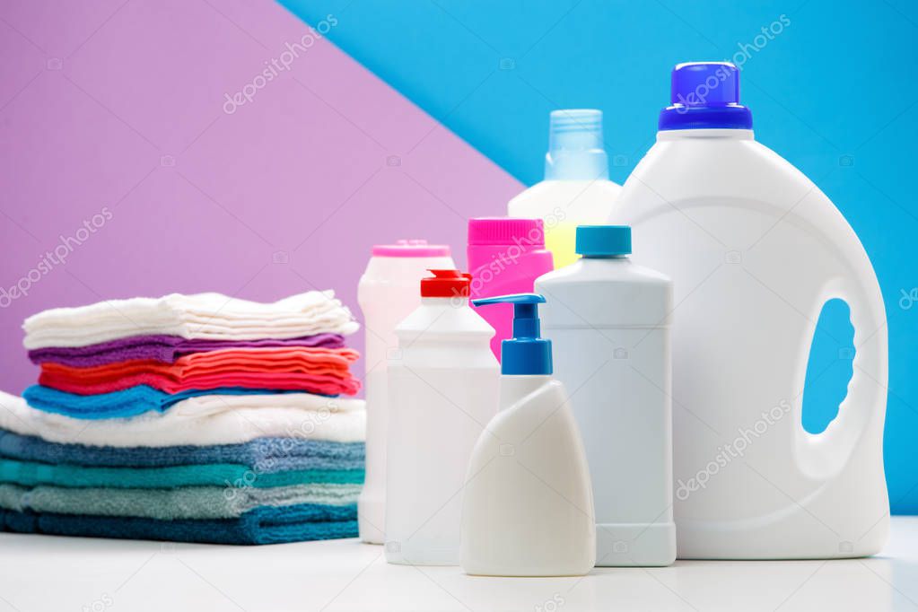 Photo of bottles of cleaning products and colored towels on white table isolated on blue, purple background