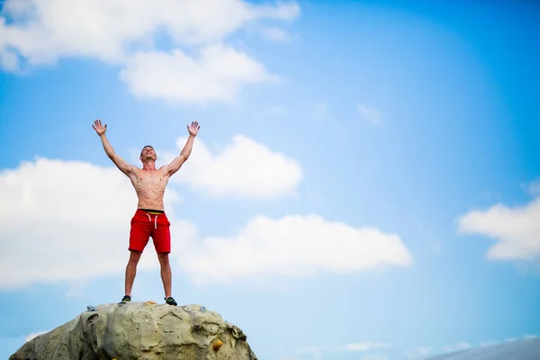 Foto de homem feliz escalador em cima de pedra contra o céu azul — Fotografia de Stock