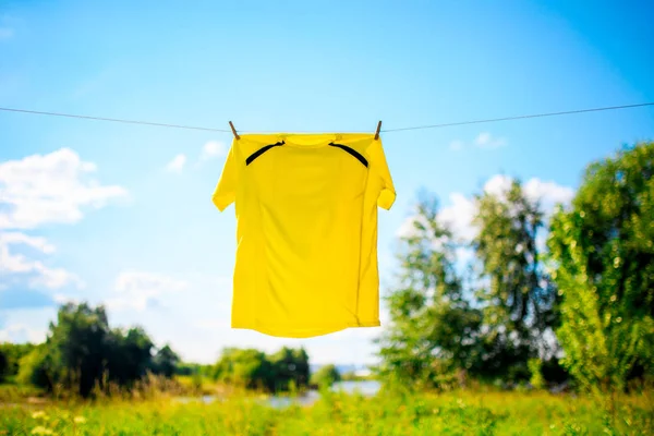 Photo of yellow T-shirt hanging on rope against blue sky with clouds