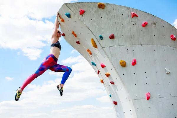 Foto de esportista em perneiras penduradas na parede para escalada contra o céu azul — Fotografia de Stock