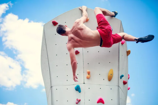 Foto von hinten von einem jungen athletischen Mann, der an einer Wand übt, um gegen blauen Himmel mit Wolken zu klettern — Stockfoto