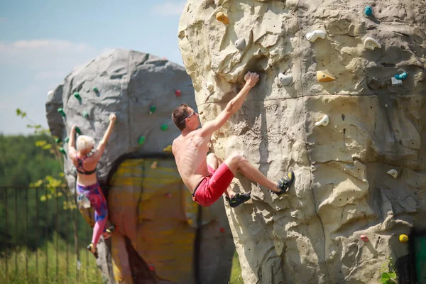 Photo of sports man in red shorts and woman on workout at climbing boulder against blue sky with clouds outdoors — Stock Photo, Image