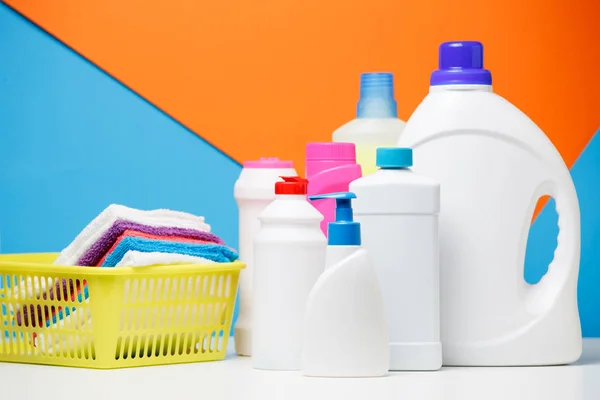 Foto de várias garrafas de produtos de limpeza e toalhas multicoloridas em cesta isolada em fundo azul, laranja — Fotografia de Stock