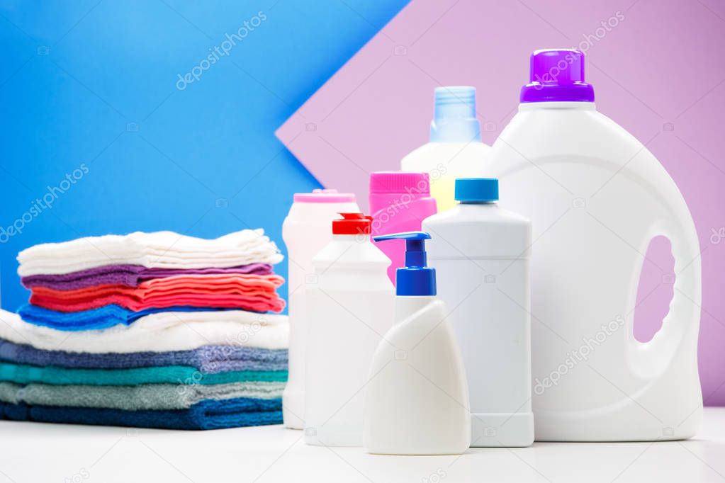 Photo of bottles of cleaning products and colored towels on table isolated on blue, purple background