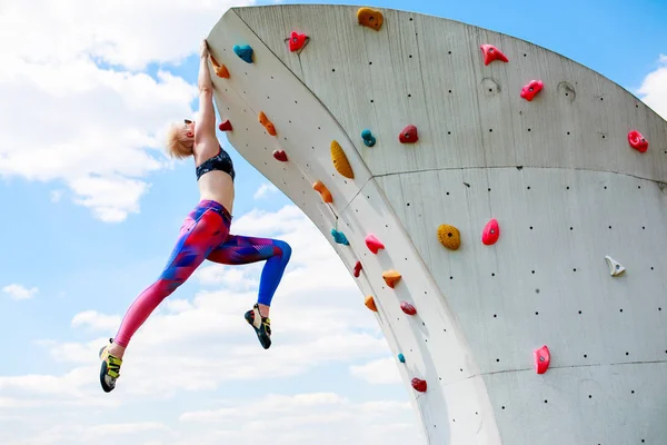 Foto de menina esportiva em leggings pendurados na parede para escalada contra o céu azul — Fotografia de Stock