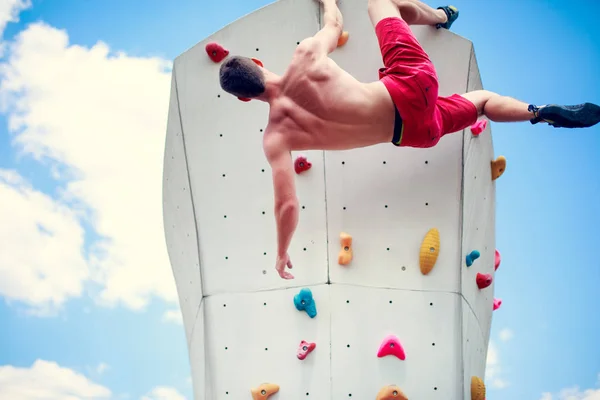 Photo from back of young athletic guy exercising on wall for climbing against blue sky with clouds — Stock Photo, Image