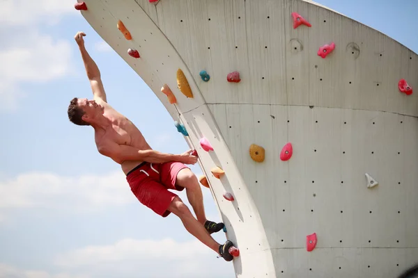 Foto eines jungen Mannes, der an einer Wand gegen bewölkten Himmel klettert — Stockfoto