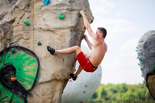 Fotografia sportowa człowieka w czerwonych spodenkach ćwiczenie na głaz do wspinaczki z pochmurnego nieba — Zdjęcie stockowe