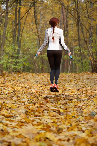 Foto ze zadní strany sportovec bruneta skákání s lanem na podzimní les — Stock fotografie