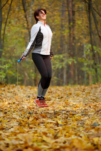 Photo of side view of sports woman jumping with rope at autumn forest — Stock Photo, Image