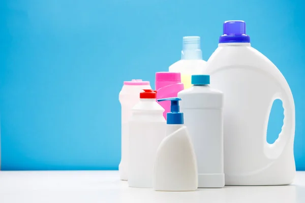 Foto de garrafas de produtos de limpeza em mesa branca isolada em fundo azul — Fotografia de Stock
