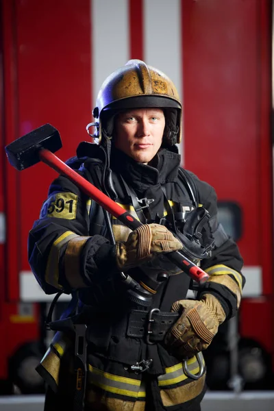 Photo of fireman with sledgehammer in hands near fire engine