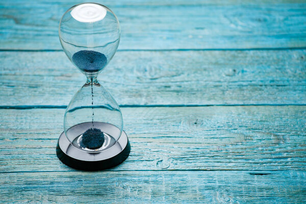 Photo of hourglass with blue sand on wooden background,