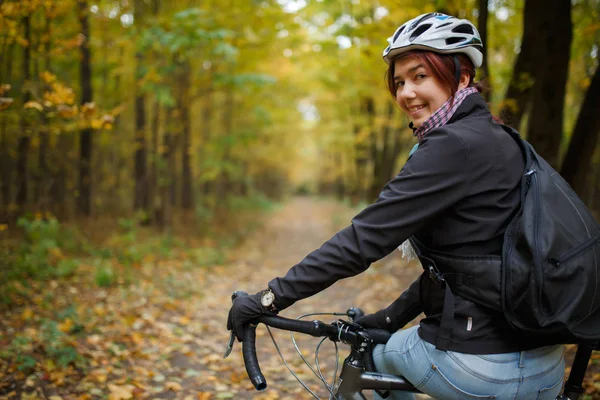 Foto di bruna sorridente in casco in bicicletta nel parco autunnale — Foto Stock