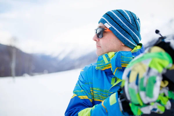 Portrait d'homme en lunettes de soleil avec snowboard dans les mains sur fond de montagnes de neige — Photo