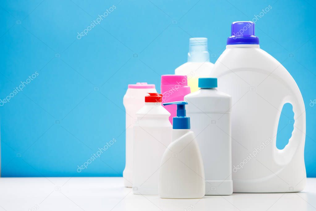 Photo of bottles of cleaning products on white table isolated on blue background