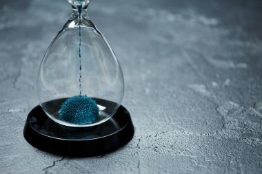 Image of hourglass with blue sand on black stone background, clipart