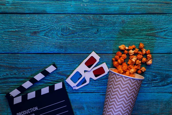 Clapperboard, glasses and popcorn on blue wooden background top view with copyspace — Stock Photo, Image