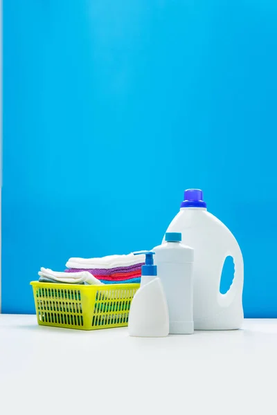 Photo of three bottles of cleansers and yellow basket with towels on empty blue background — Stock Photo, Image