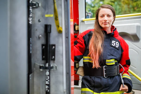 Foto de mujer de fuego con el pelo largo en overoles se levanta en el coche de bomberos — Foto de Stock