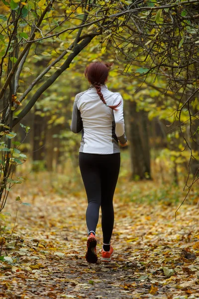 Φωτογραφία από πίσω νεαρή γυναίκα τρέχει μέσα από το πάρκο φθινόπωρο — Φωτογραφία Αρχείου