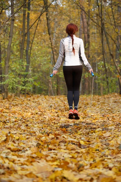 Foto de la espalda de la morena de los deportes saltando con cuerda en el bosque de otoño —  Fotos de Stock