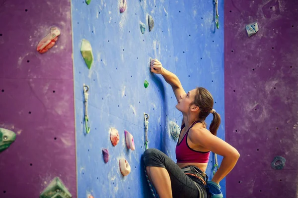 Фото спортивної жінки з сумкою для розмов позаду, яка тренується на скелелазінні стінки — стокове фото