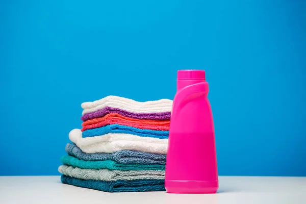 Photo of one pink bottle of cleanser and stack of colored towels isolated background — Stock Photo, Image