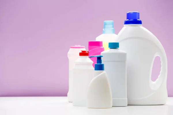 Foto di bottiglie di prodotti per la pulizia su tavolo bianco isolato su sfondo viola — Foto Stock