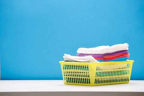 Zdjęcie z ręczniki wielobarwne w żółty koszyk na pusty niebieskie tło. — Zdjęcie stockowe