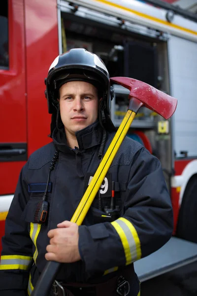 Foto de bombeiro sério com machado no fundo do carro de bombeiros — Fotografia de Stock