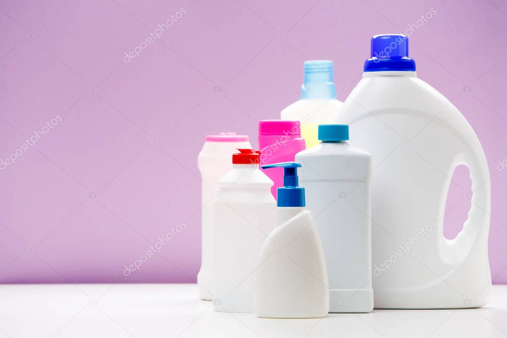 Photo of bottles of cleaning products on white table isolated on purple background