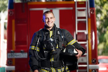 Photo of happy fireman with gas mask and helmet near fire engine clipart