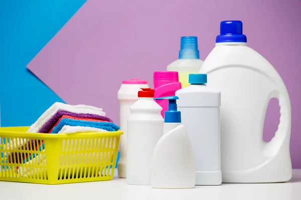 Foto de varias botellas de detergentes y toallas multicolores en cesta aislada sobre fondo púrpura, azul — Foto de Stock