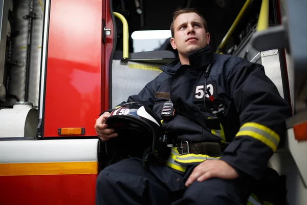 Foto eines jungen Feuerwehrmannes mit Helm in der Hand, der im Feuerwehrauto sitzt — Stockfoto