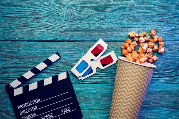 Clapperboard, glasses and popcorn on blue wooden background top view with copyspace — Stock Photo, Image