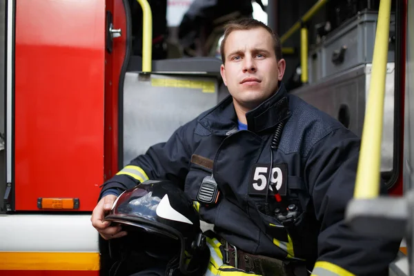 Foto hasič s helmou v ruce sedí v rudý oheň motoru — Stock fotografie