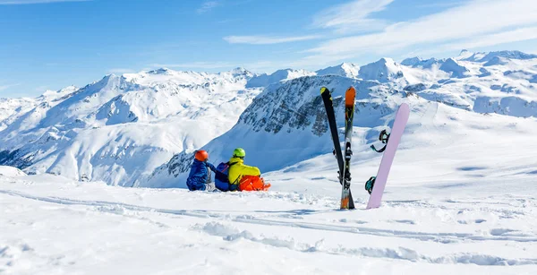 Snowboarder und Skifahrer sitzen auf Schnee und sehen in den Bergen — Stockfoto