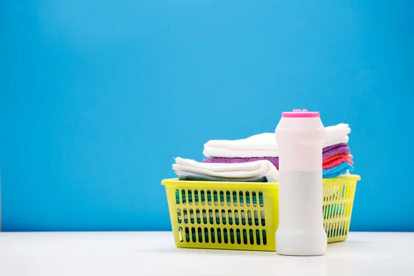 Foto de uma garrafa de pó de limpeza e toalhas multicoloridas em cesta isolada em fundo azul — Fotografia de Stock