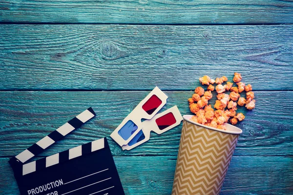 Clapperboard, glasses and popcorn on blue wooden background top view with copyspace — Stock Photo, Image