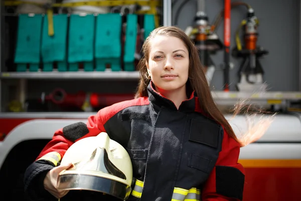 Foto de una joven bombera mirando a la cámara con el pelo largo junto al camión de bomberos —  Fotos de Stock