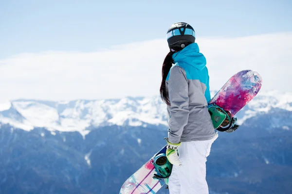 Foto dal retro del casco turistico donna con snowboard sullo sfondo di montagne innevate — Foto Stock