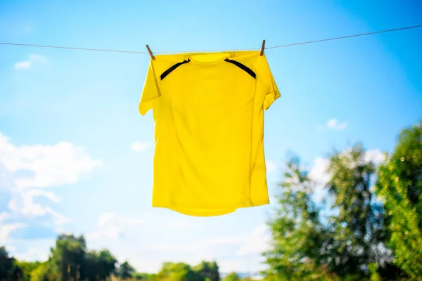 Photo of yellow T-shirt hanging on rope against blue sky background