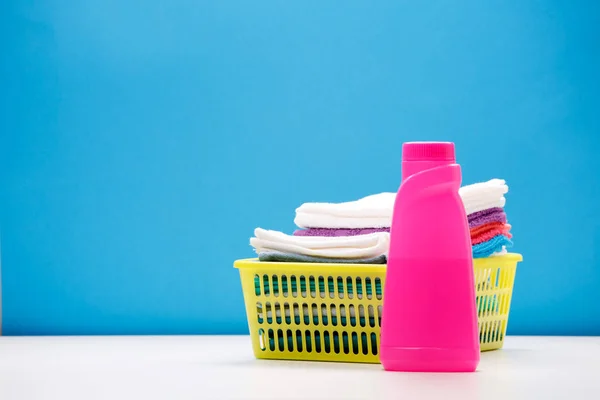 Photo of one pink bottle of detergent and colored towels in basket isolated on blue background — Stock Photo, Image