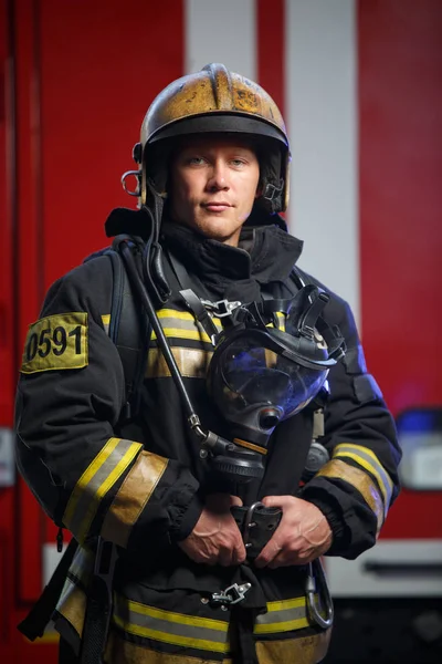 Foto do jovem bombeiro usando capacete com máscara de gás no fundo do carro de bombeiros — Fotografia de Stock