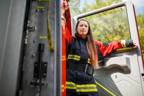 Foto der jungen Feuerwehrfrau mit langen Haaren in Overalls steht im Feuerwehrauto — Stockfoto