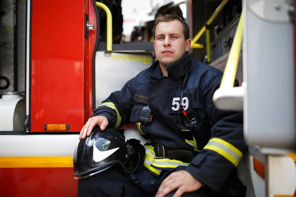Foto de jovem bombeiro com capacete em macacão senta-se em caminhão de bombeiros — Fotografia de Stock