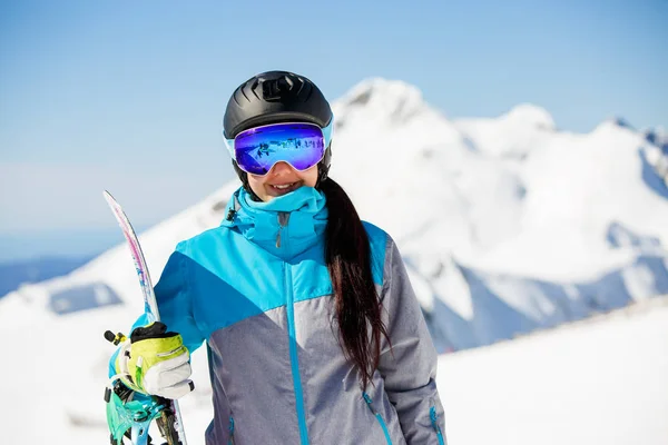 Photo de jeune femme en casque portant des lunettes de soleil, avec snowboard sur fond de montagnes de neige — Photo