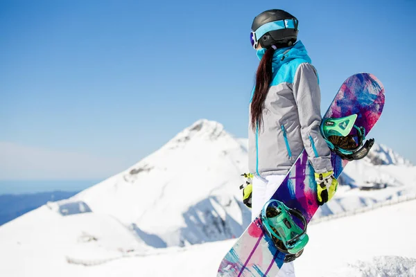 Foto de lado de la mujer casco turístico con snowboard en el fondo de las montañas de nieve —  Fotos de Stock