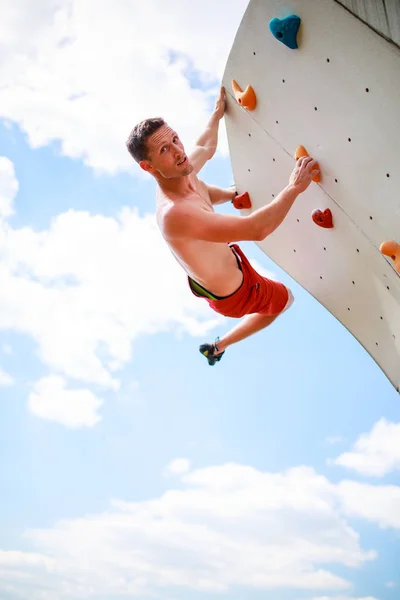 Foto des Athleten mit Blick auf die Kamera, der an der Wand übt, um vor blauem Himmel mit Wolken zu klettern — Stockfoto